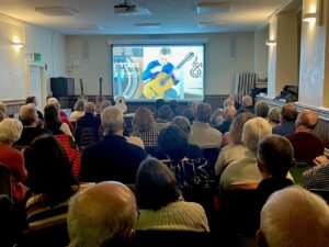 The audience watching a video clip of one of David's guitars being played